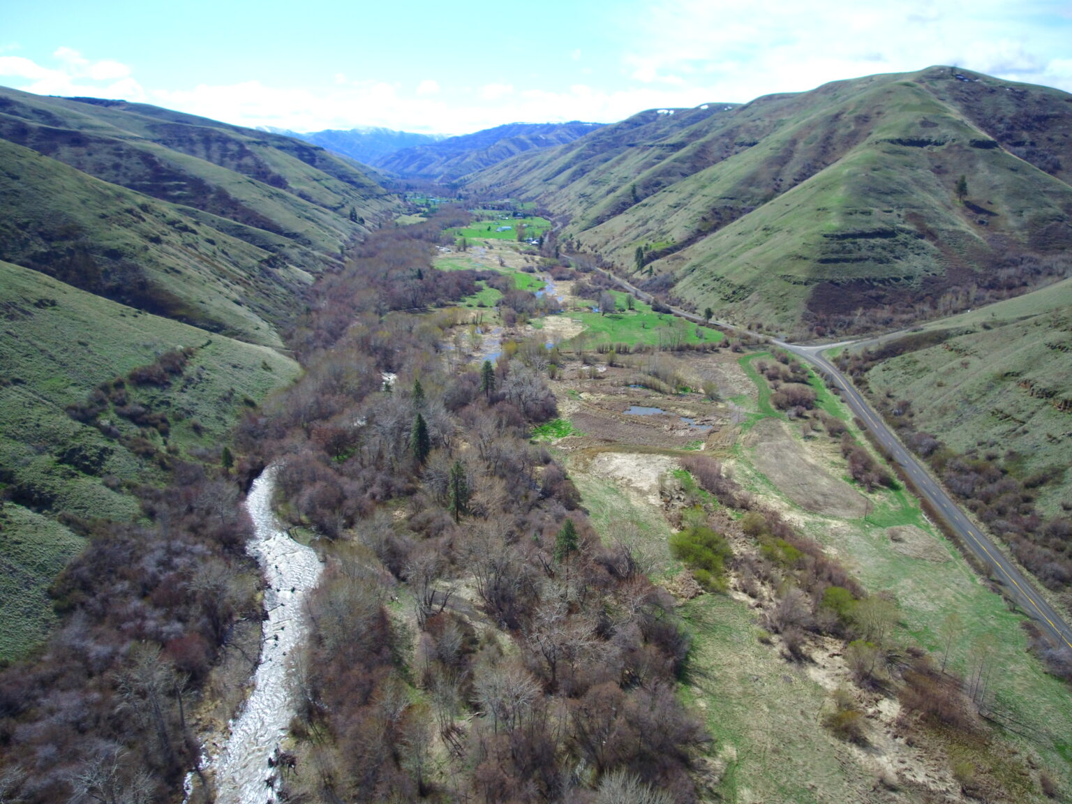 Aerial view of a green valley with a river, road, and sparse vegetation.