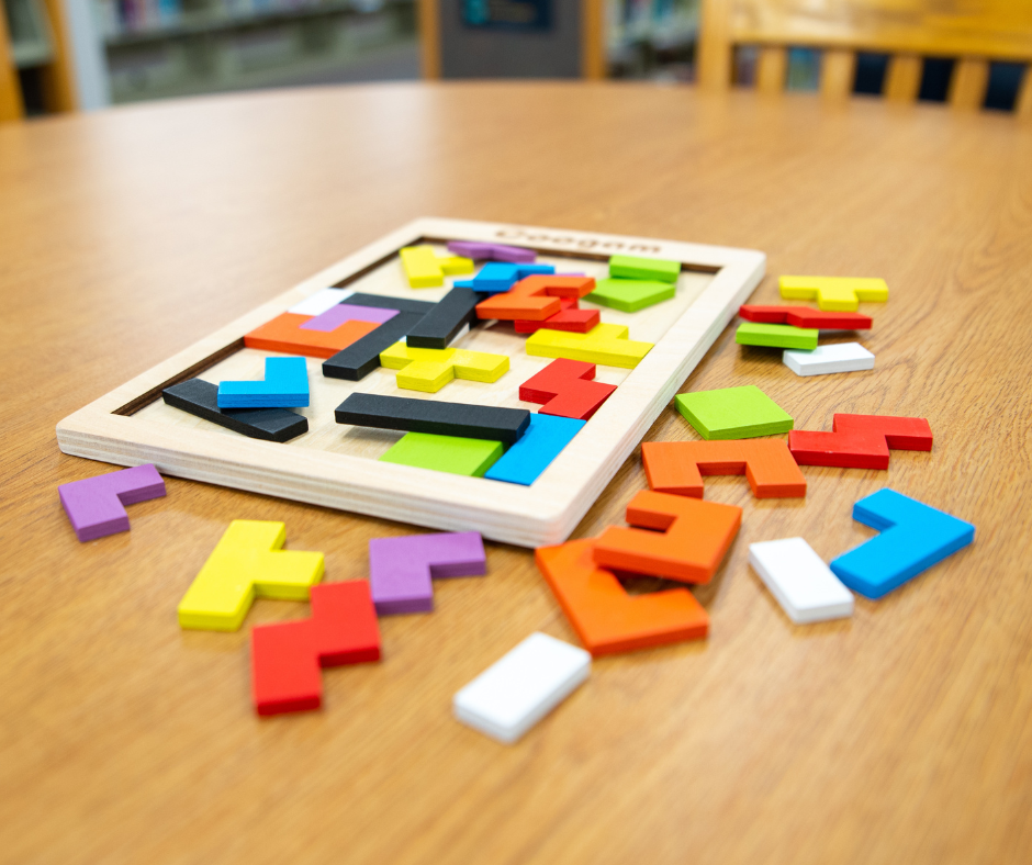 A colorful wooden puzzle with various geometric pieces scattered around and some fitting into a wooden frame on a table.