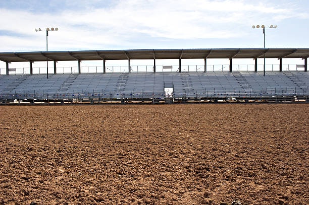 Empty outdoor rodeo arena with stadium seating and a dirt ground.