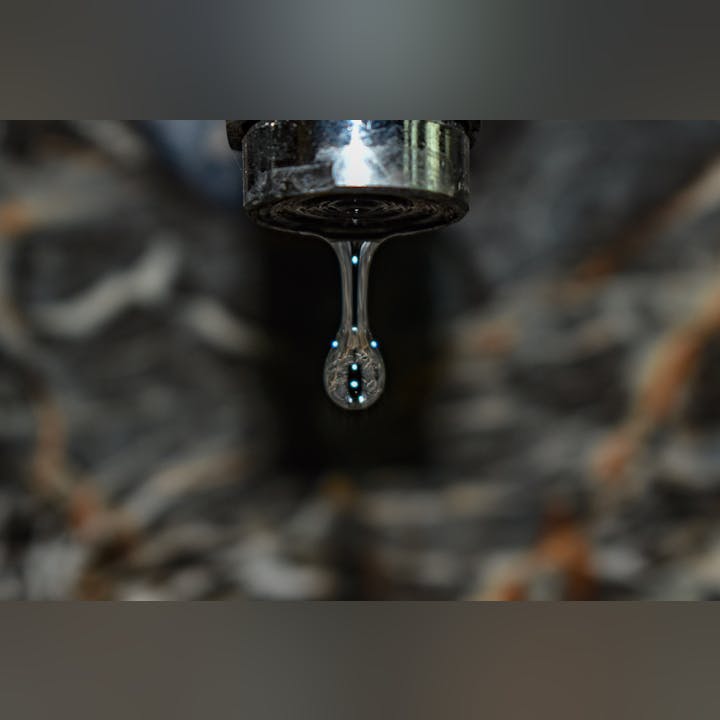 A water droplet is hanging from a faucet, about to fall.