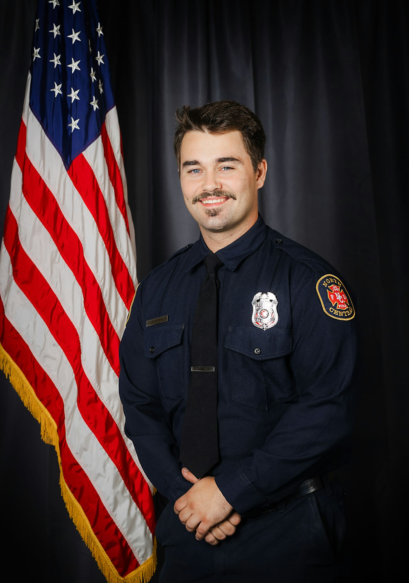 A smiling person in firefighter uniform in front of the US flag.