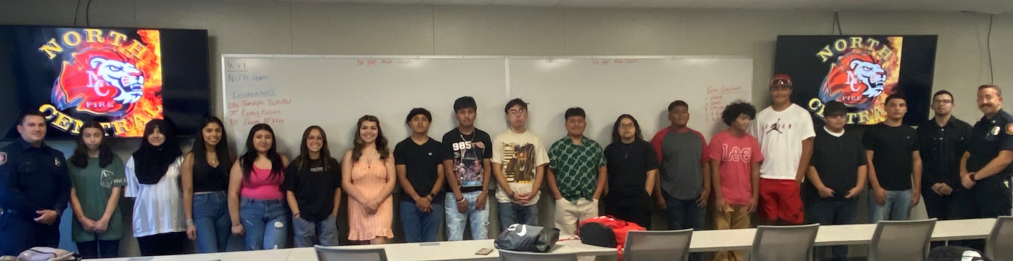 A group of people, including students and firefighters, standing in front of a whiteboard with "North Central Fire" logos displayed.