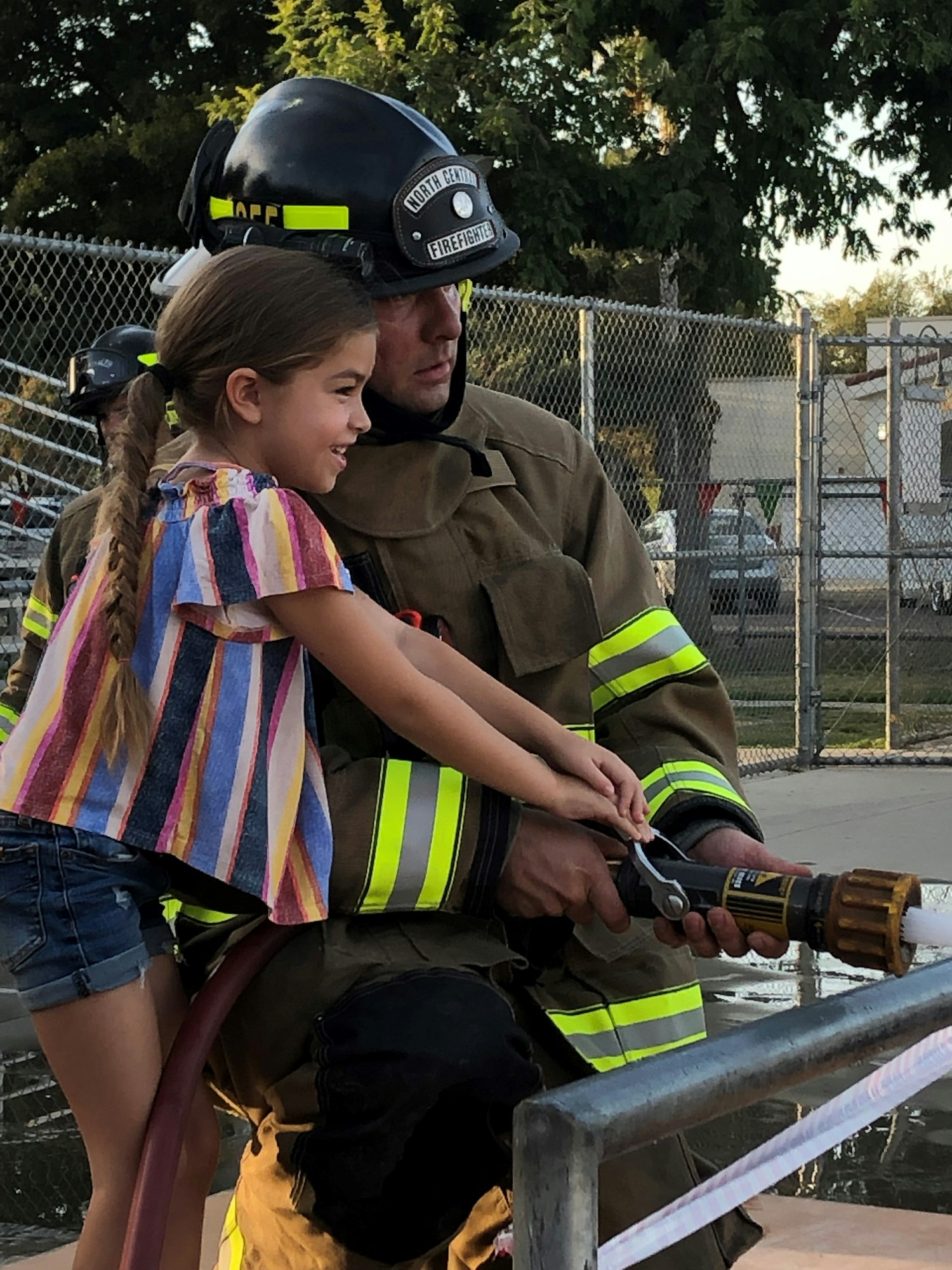 fireman helping a little girl spray a fire hose.