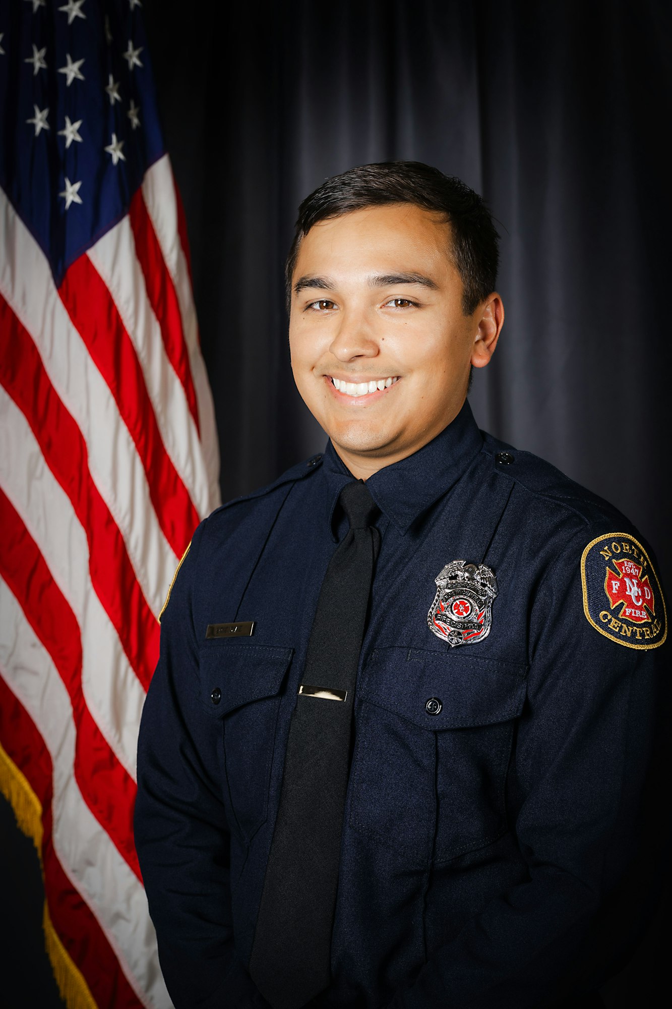 Smiling person in a firefighter uniform with an American flag background.