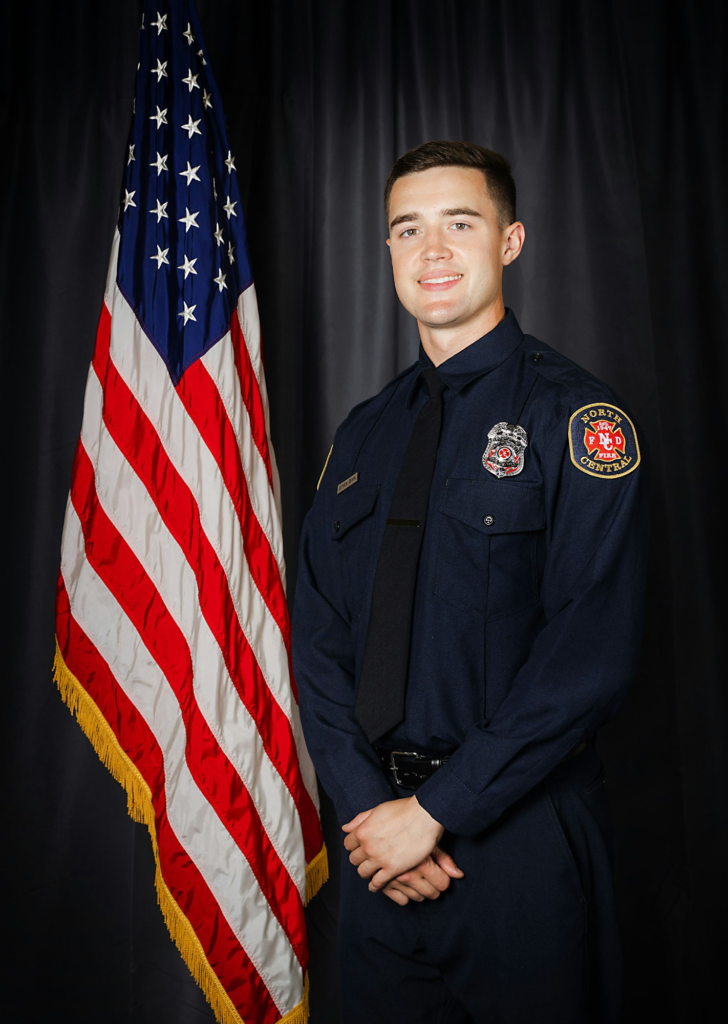 A person in a firefighter uniform stands next to an American flag.
