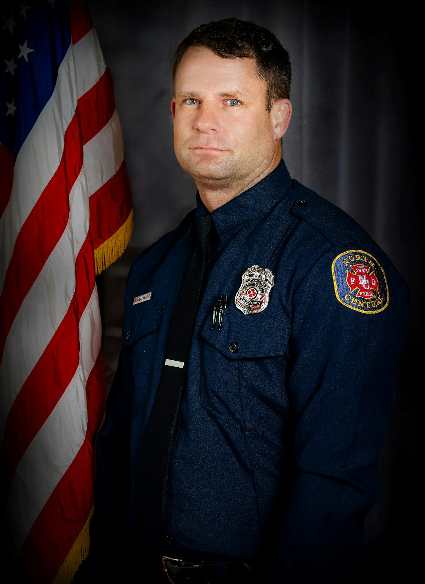 A firefighter in uniform poses next to an American flag.