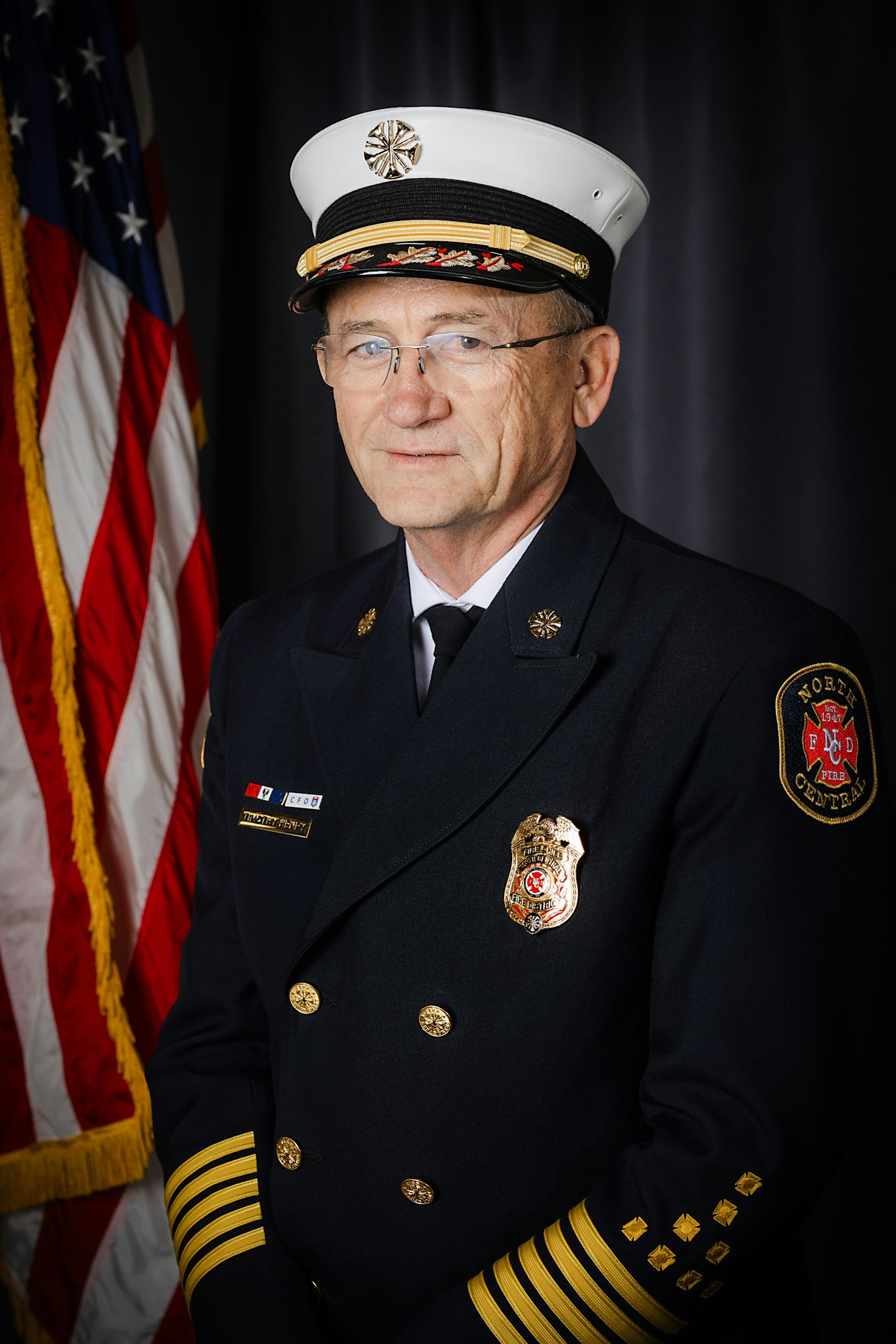 Fire Chief Henry in uniform with a badge and cap, in front of the US flag.