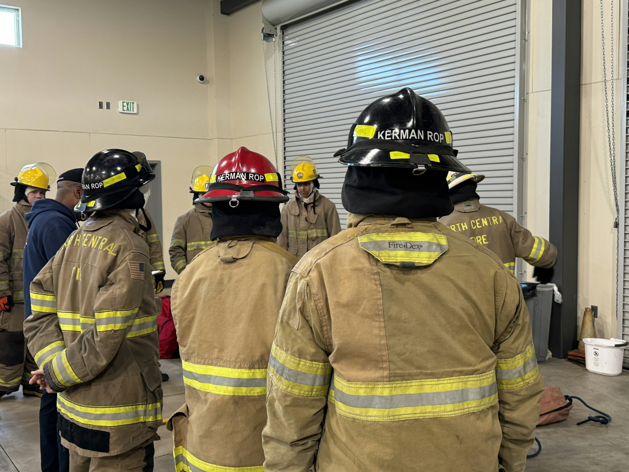 Group of firefighters in protective gear inside a building with a roll-up door.