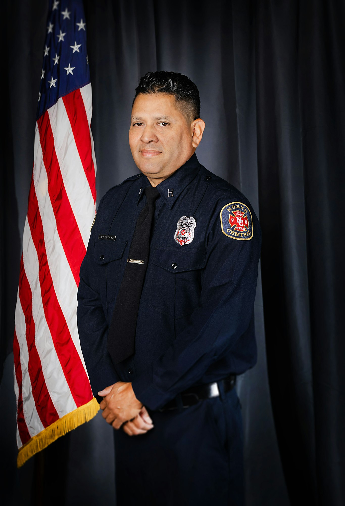 Fire Captain Vasquez in uniform stands in front of the American flag.