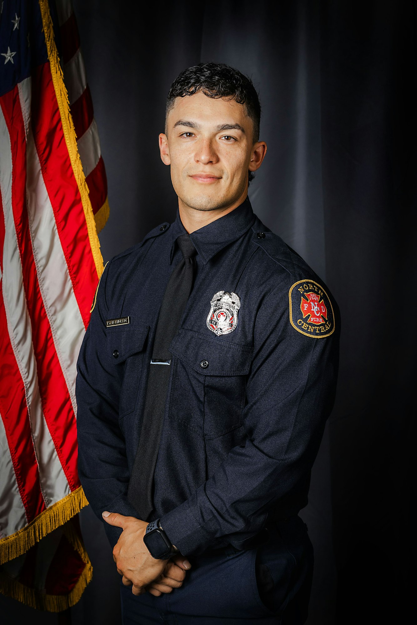 A firefighter in uniform posing in front of an American flag.
