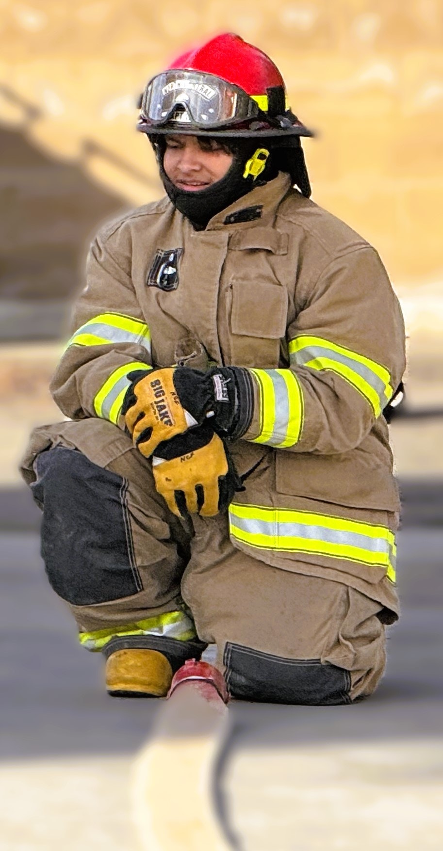 A firefighter kneeling with helmet and protective gear, holding a hose.