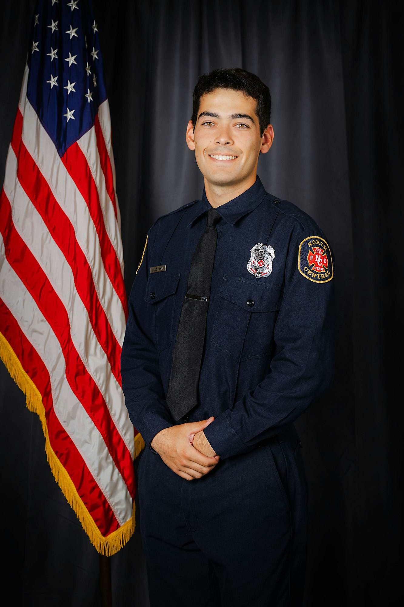 A smiling person in a firefighter's uniform stands in front of the American flag.
