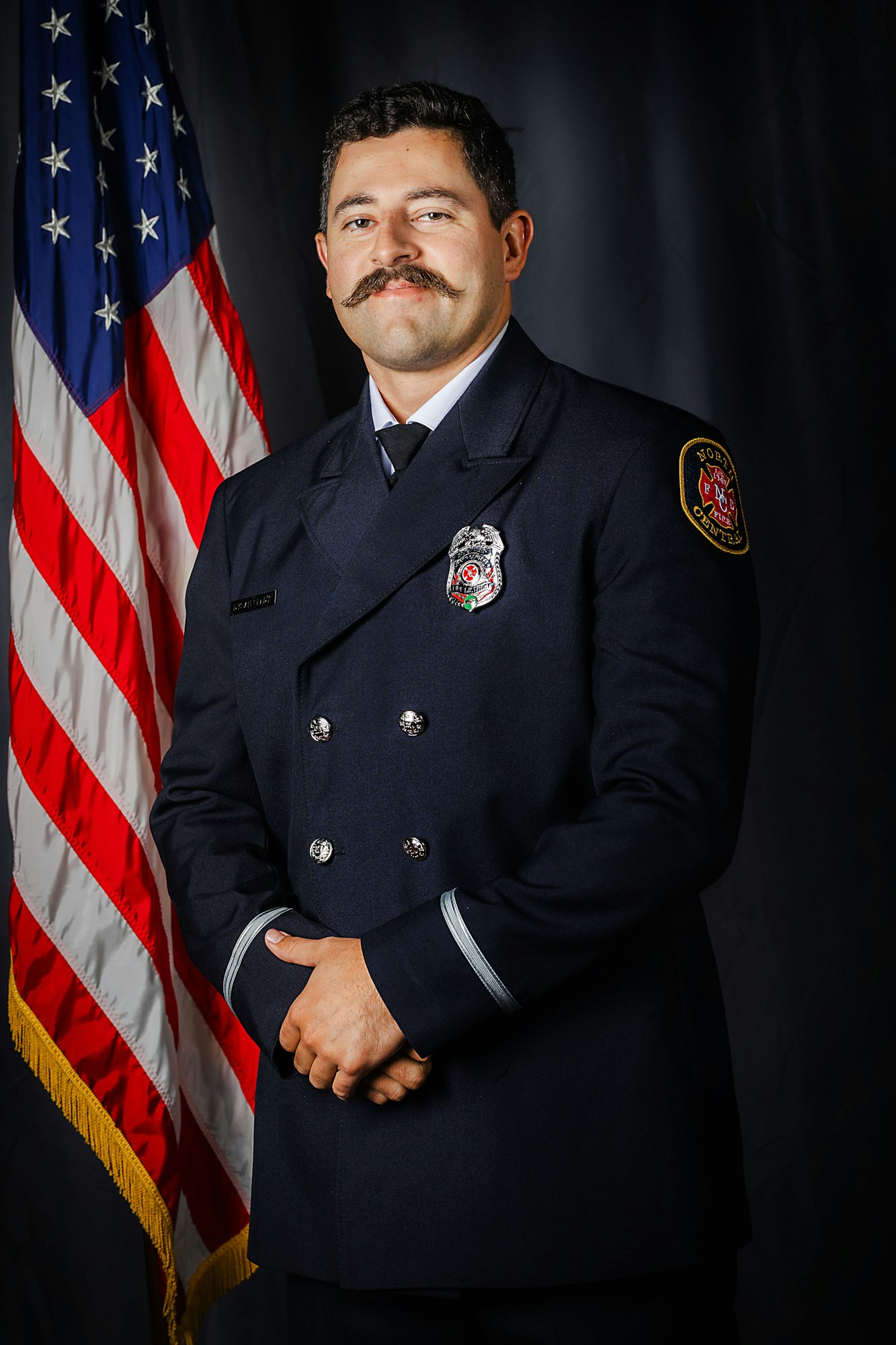 A firefighter in uniform stands before an American flag.