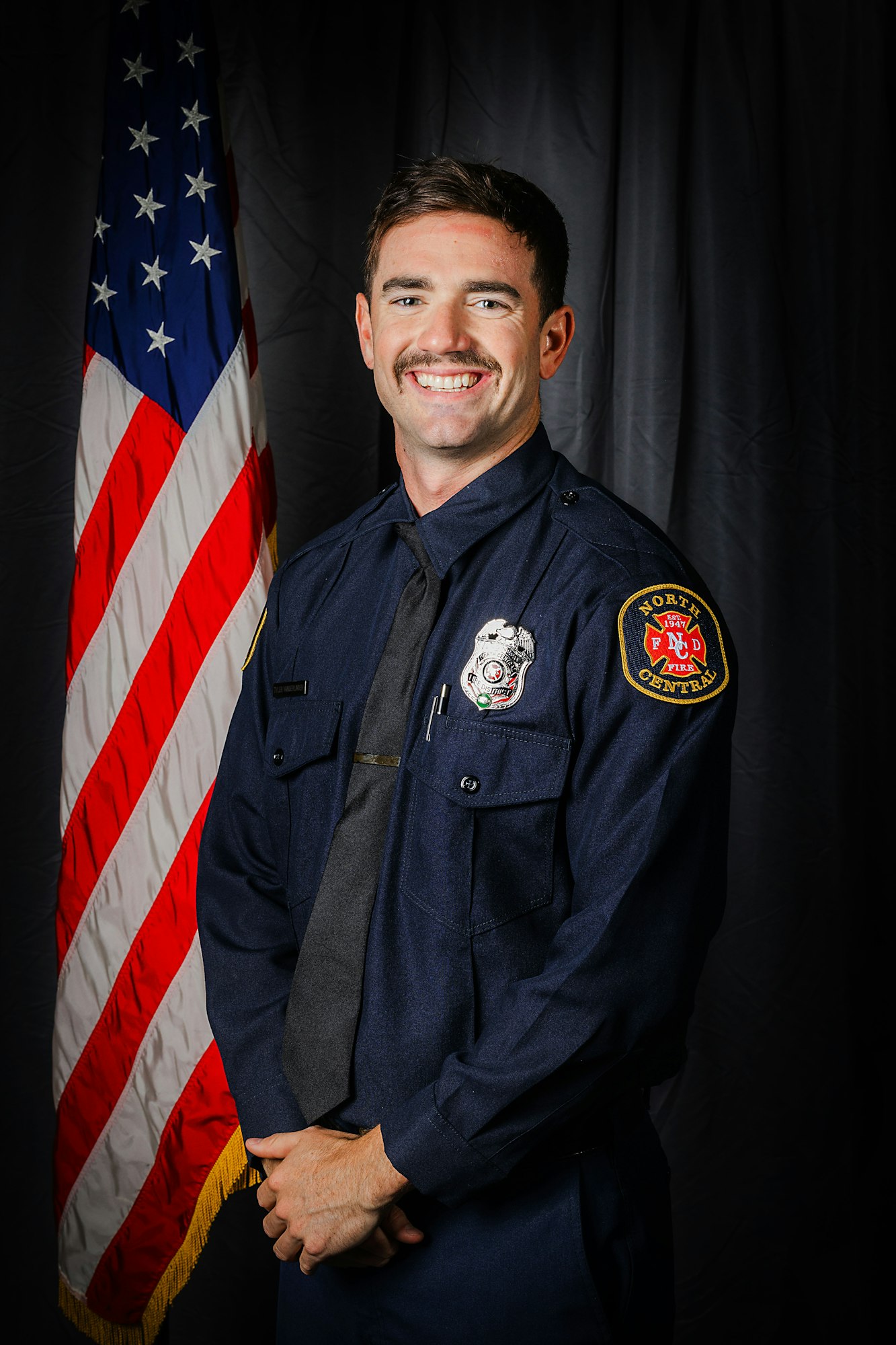 A smiling firefighter in uniform in front of the American flag.