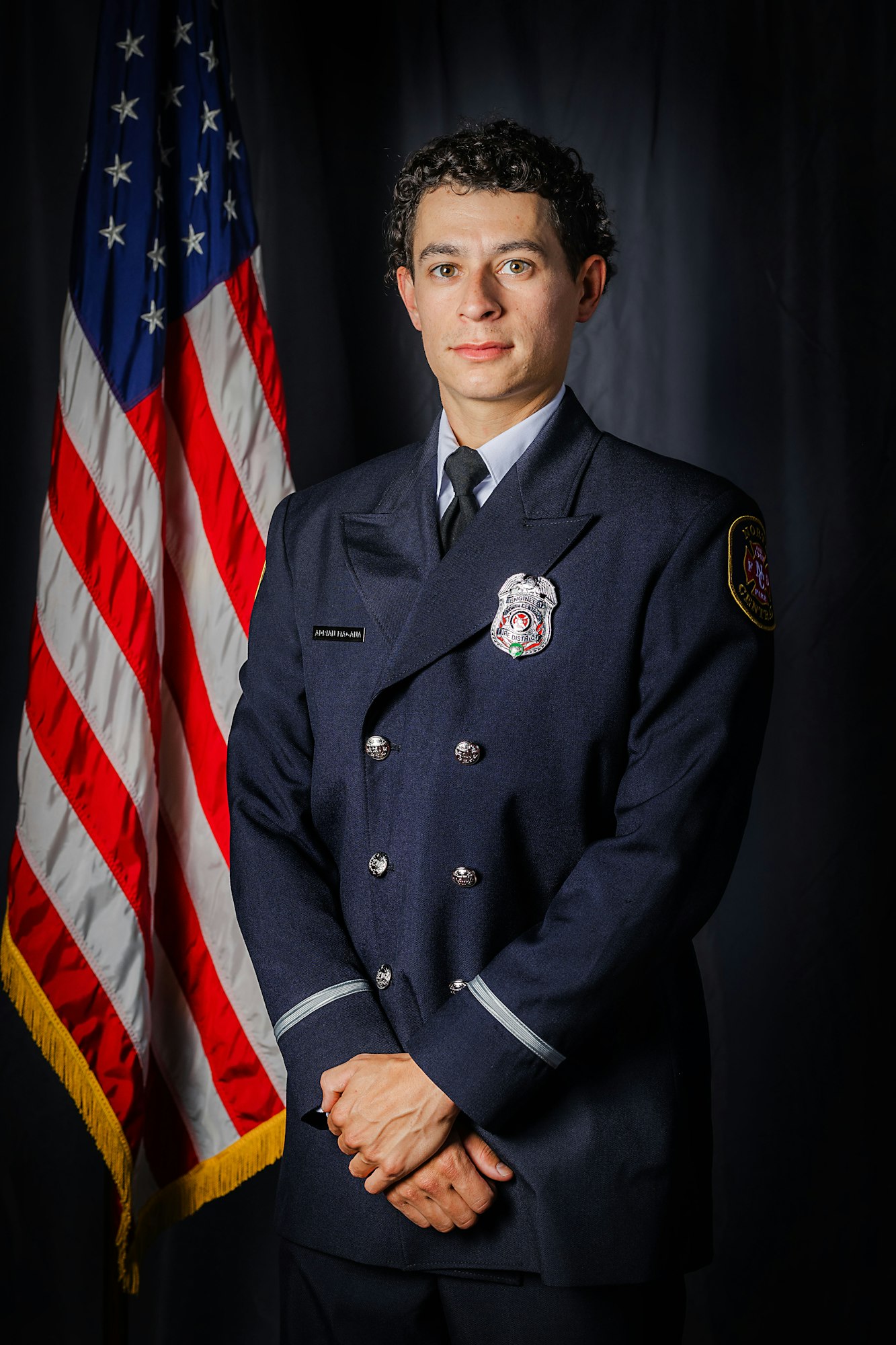 A person in a formal uniform with an American flag in the background.