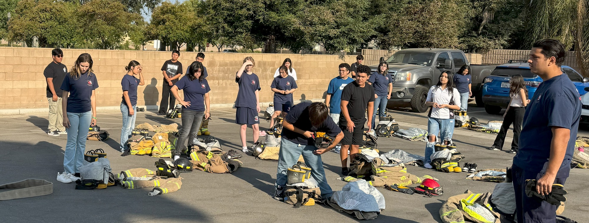 A group of people standing outdoors with fire gear on the ground, possibly in training or a drill session.