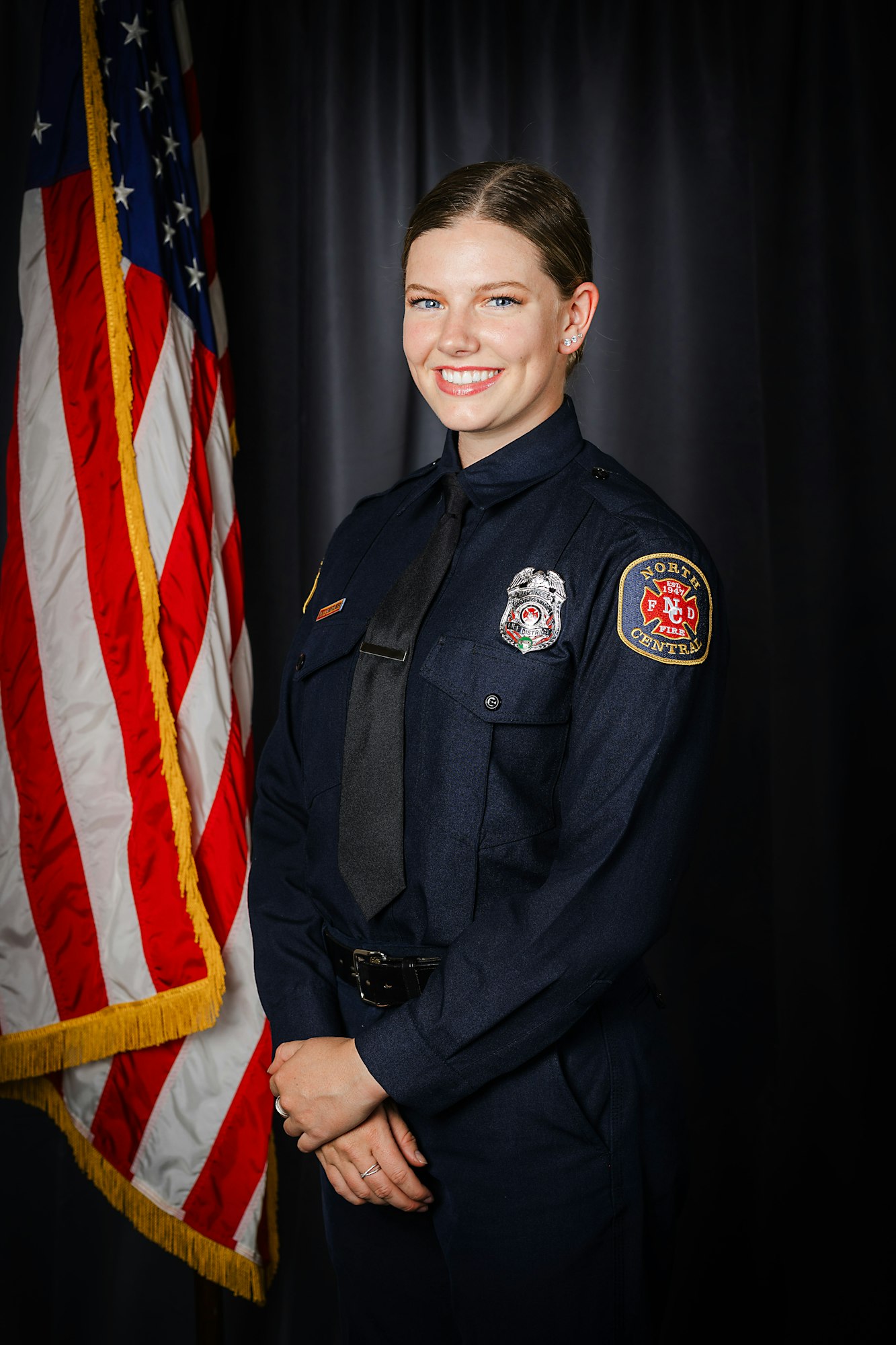 A smiling woman in a firefighter uniform in front of the American flag.