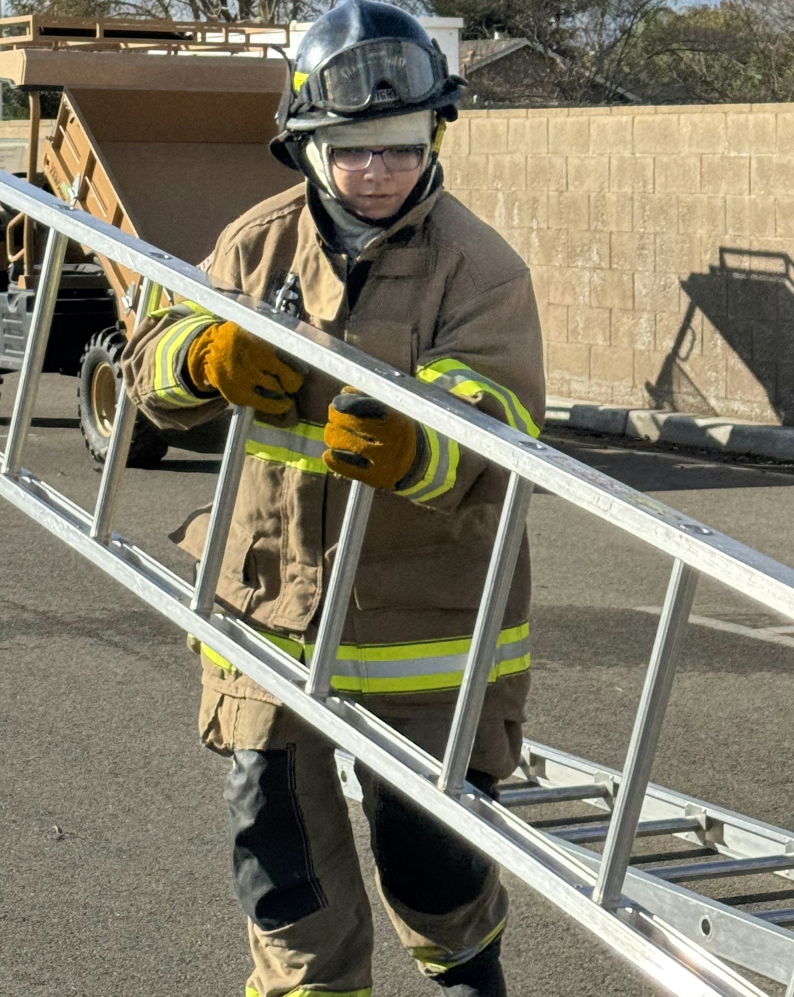A firefighter wearing protective gear is moving a ladder outdoors.