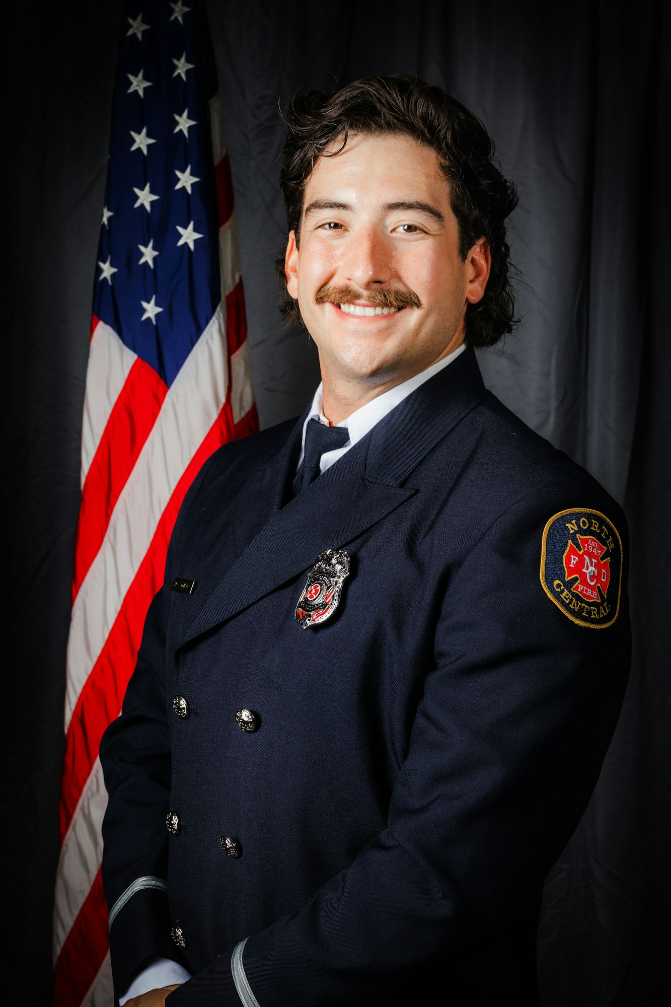 A smiling person in firefighter uniform in front of the American flag.