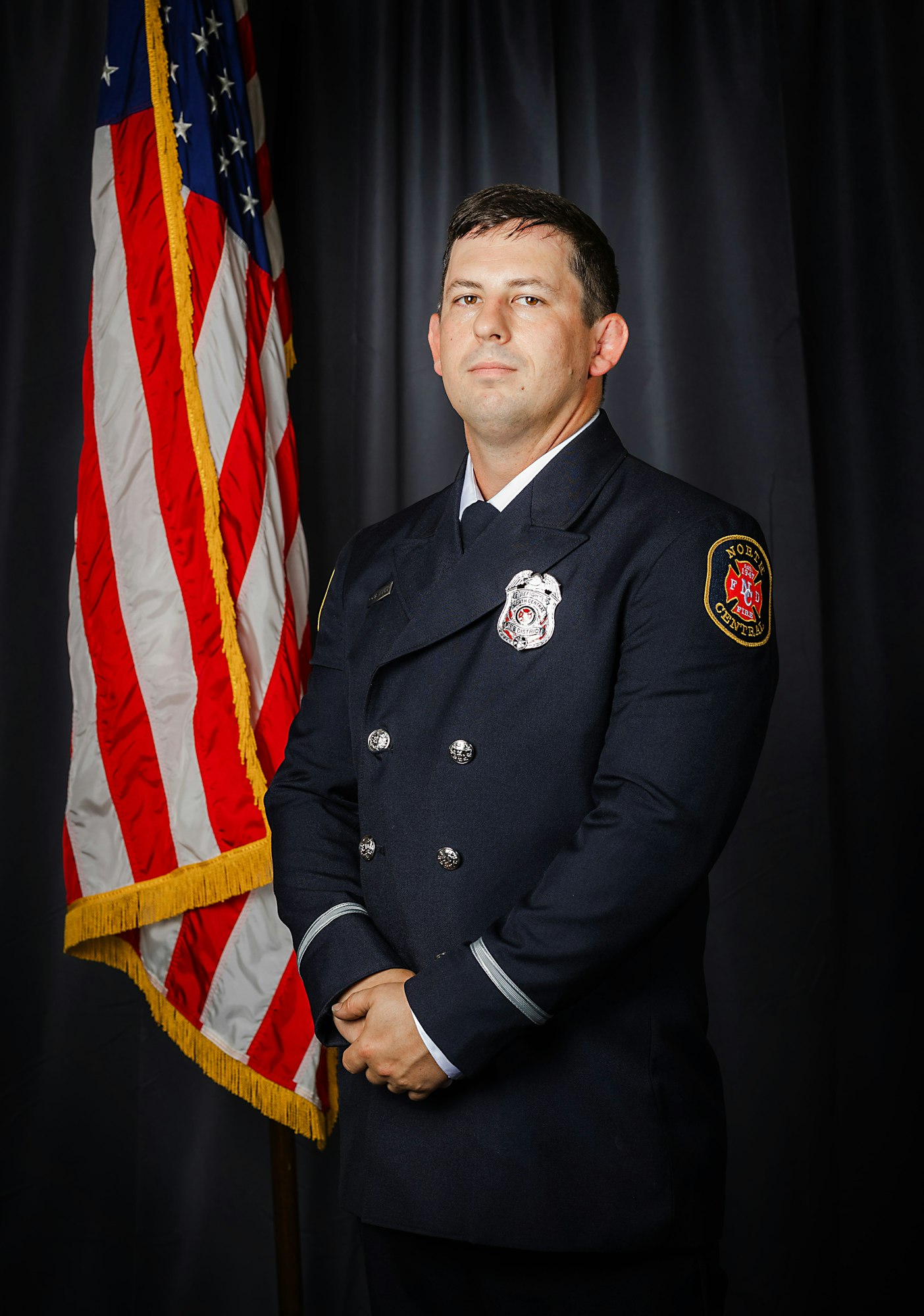 A uniformed firefighter standing proudly in front of the American flag.