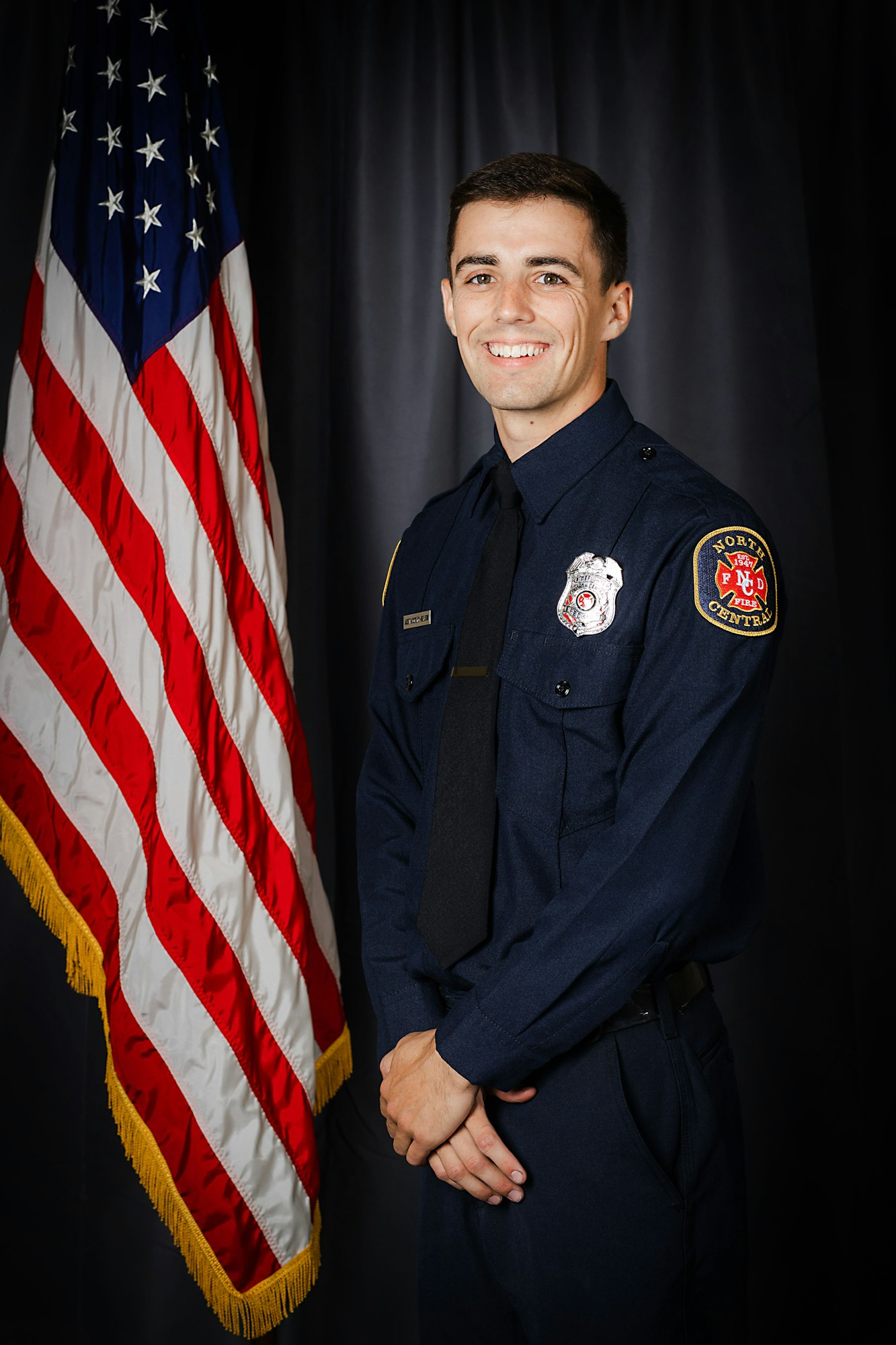 A smiling person in a firefighter's uniform in front of the American flag.