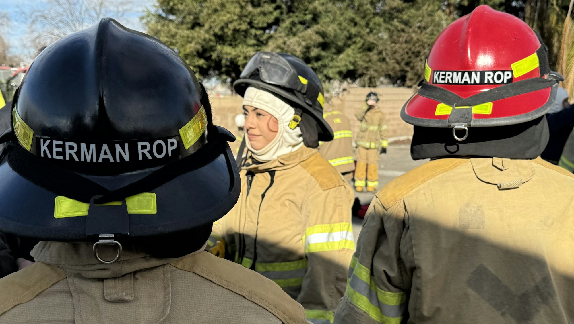 Firefighters in gear with helmets labeled "Kerman ROP" standing together outdoors.
