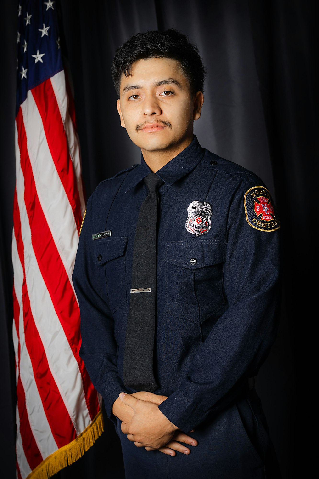 A person in a firefighter uniform stands in front of an American flag.