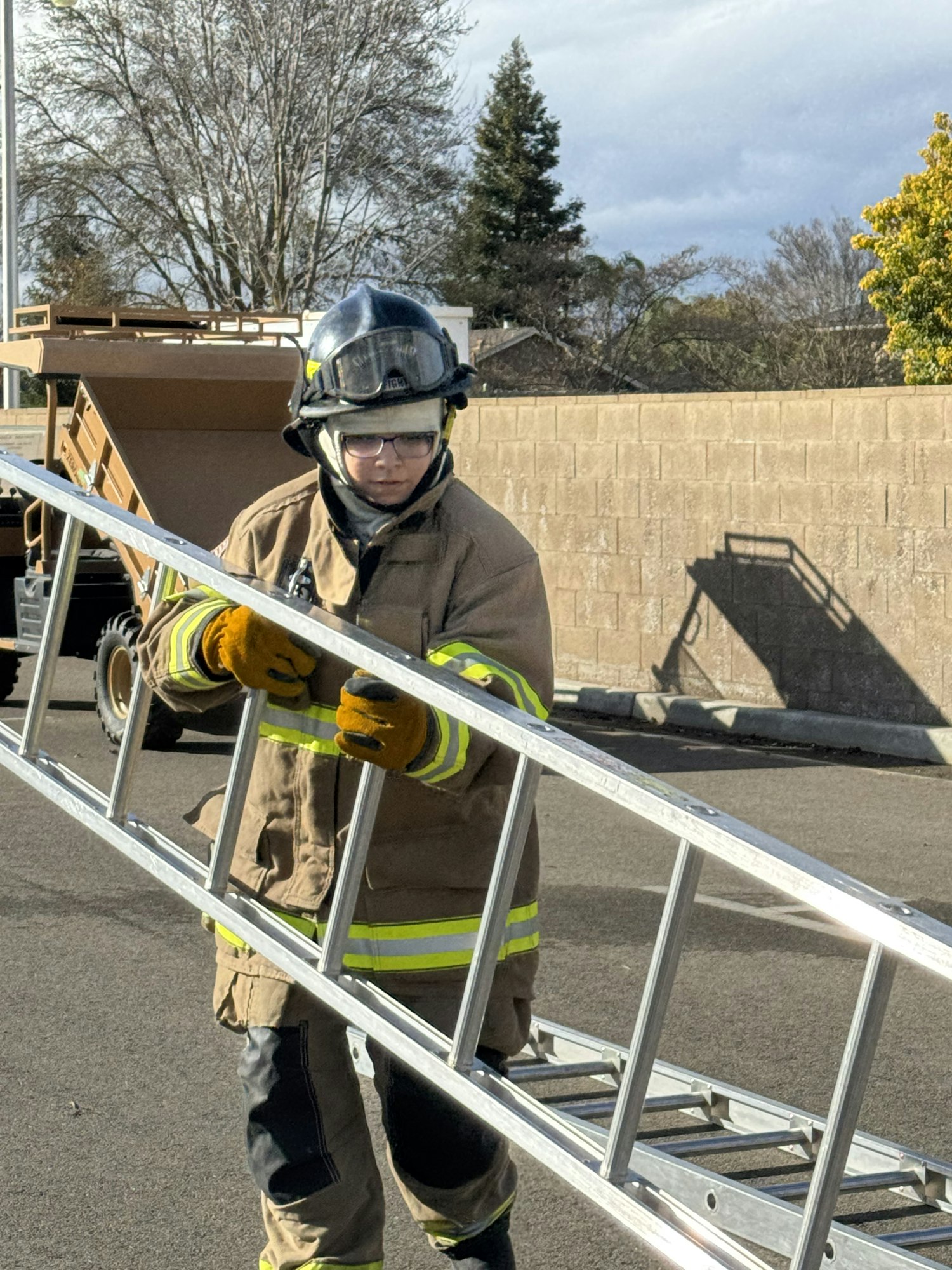 A firefighter in gear is holding a metal ladder outdoors.