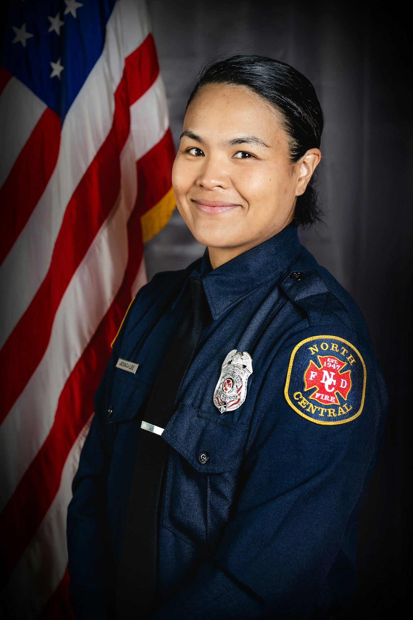 Jessica Lee in a firefighter uniform beside an American flag.
