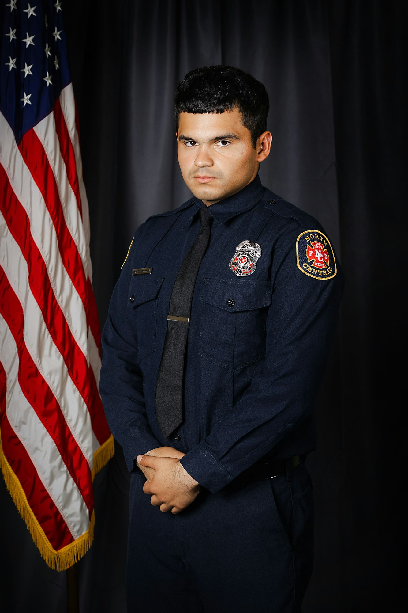 A person in a firefighter uniform stands before an American flag.