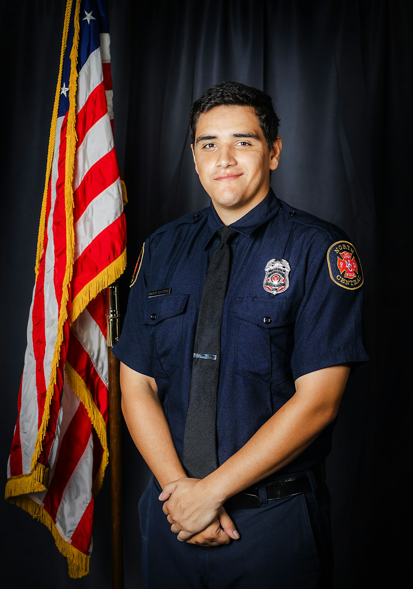 A person in a firefighter uniform standing by the US flag.