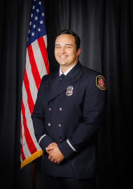 Fire Engineer Papaleo in uniform posing in front of the American flag.