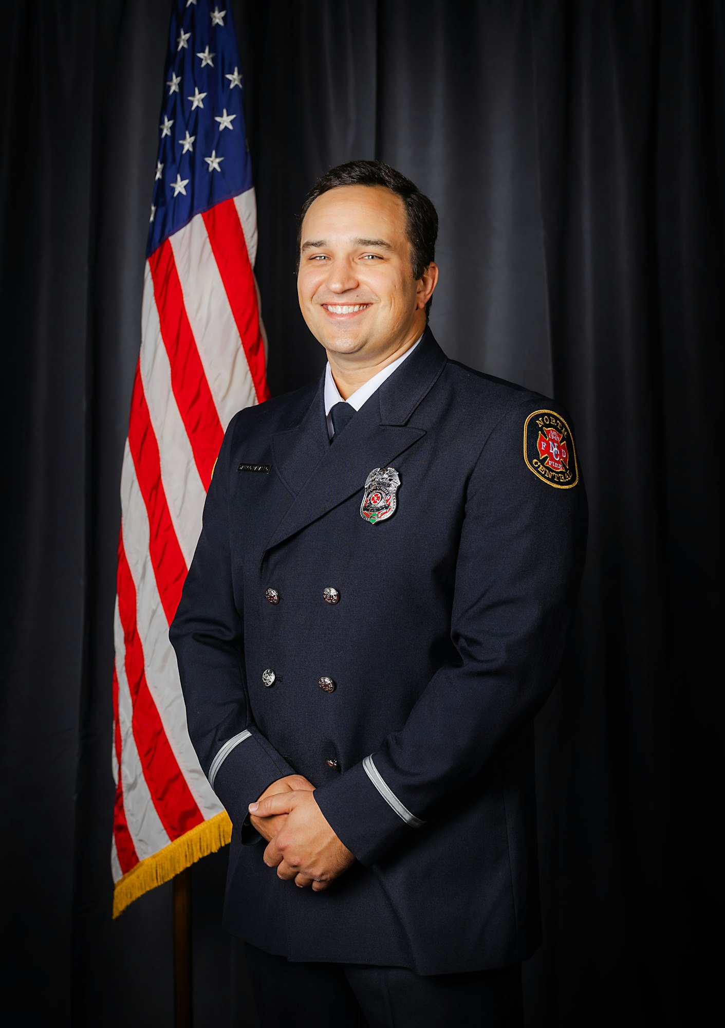 Fire Engineer Papaleo in uniform posing in front of the American flag.