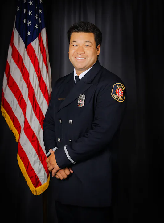 Fire Engineer Lum in uniform posing in front of the American flag.