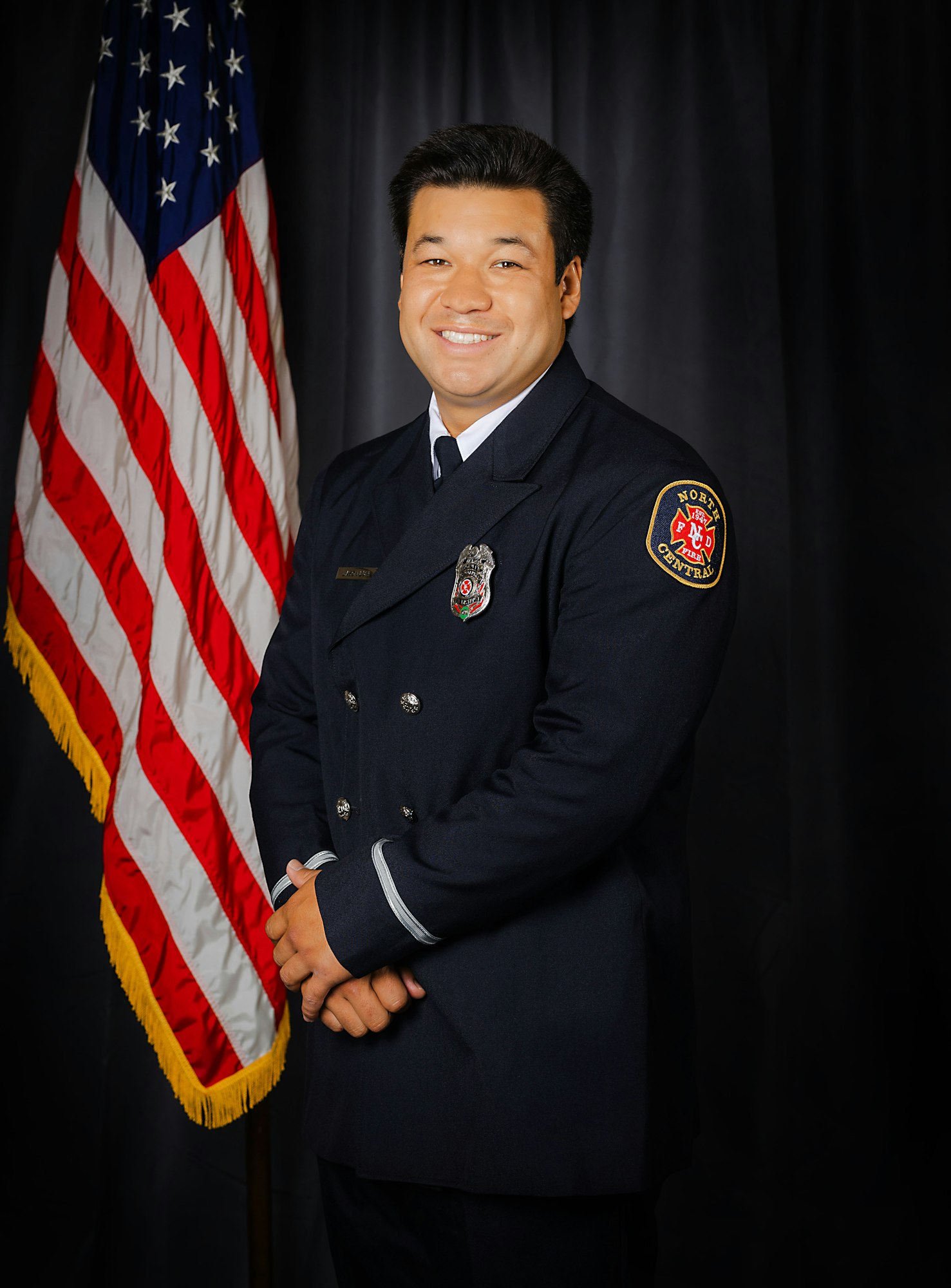 Fire Engineer Lum in uniform posing in front of the American flag.