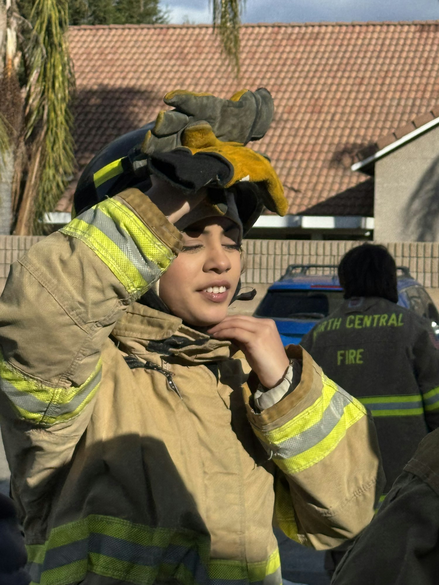 A person in firefighter gear adjusting their helmet, with others in the background.