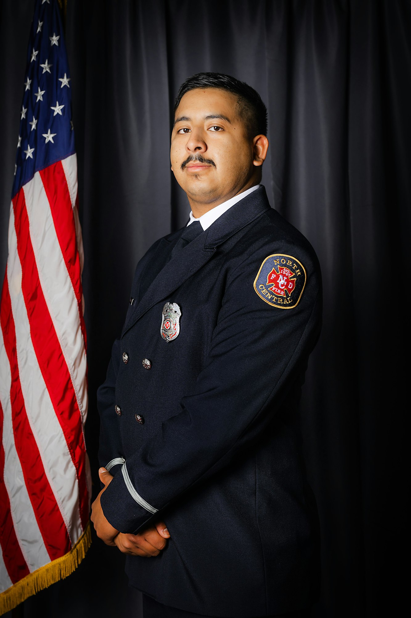 A man in a firefighter's uniform stands proudly before an American flag.