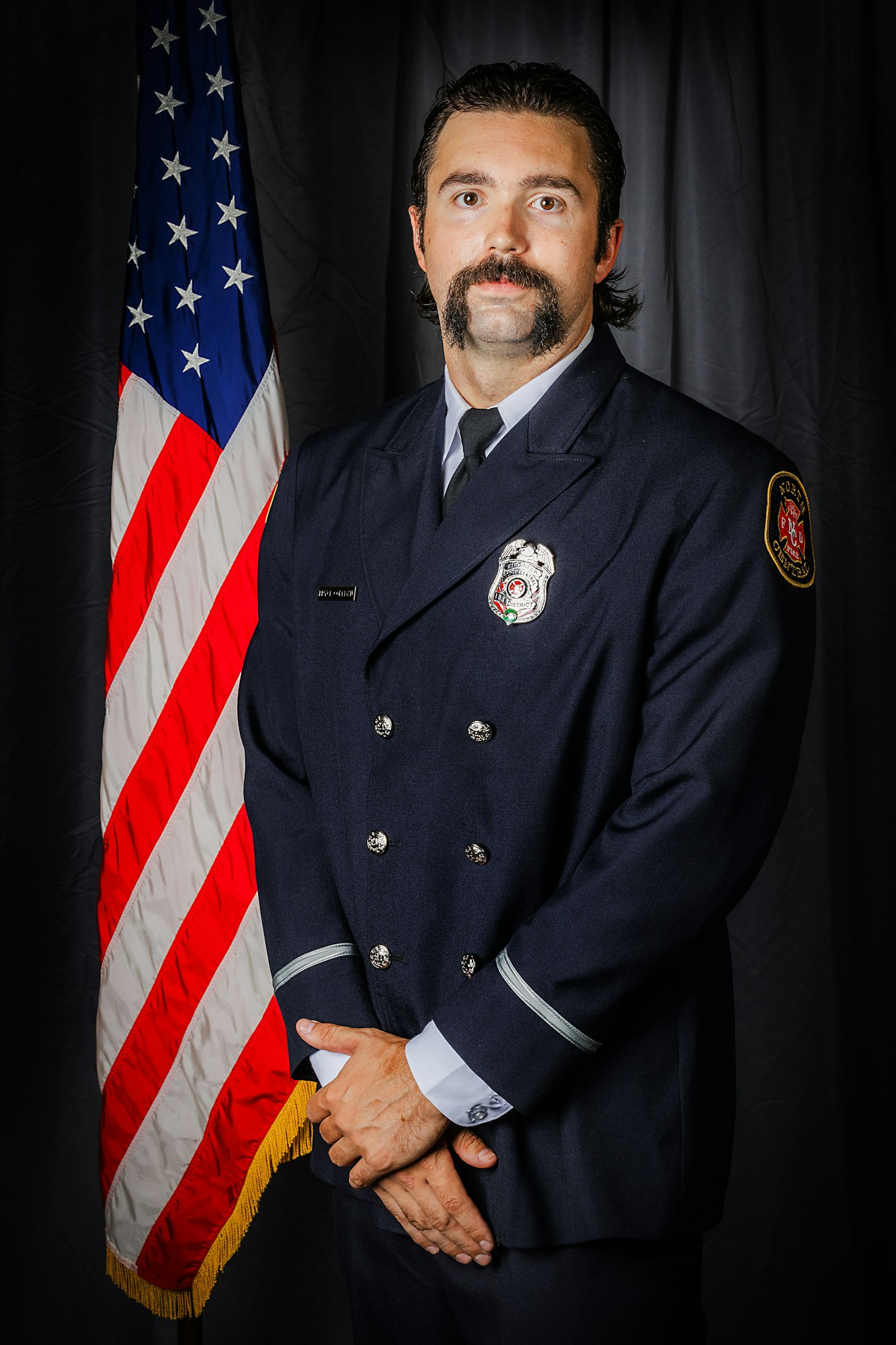 Fire Engineer Coleman in uniform stands proudly before the American flag.