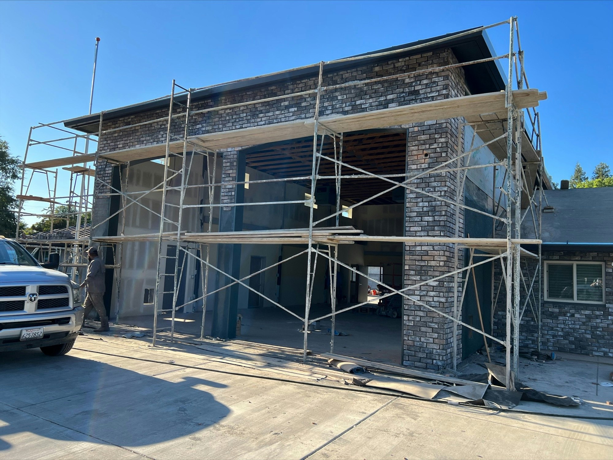 A construction site with scaffolding around a building, featuring brick walls and an ongoing renovation, under a clear blue sky.