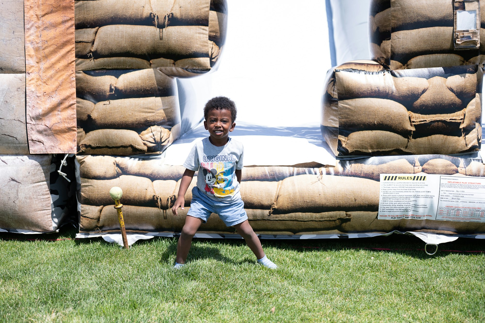 A child smiling in front of an inflatable structure, standing on grass.