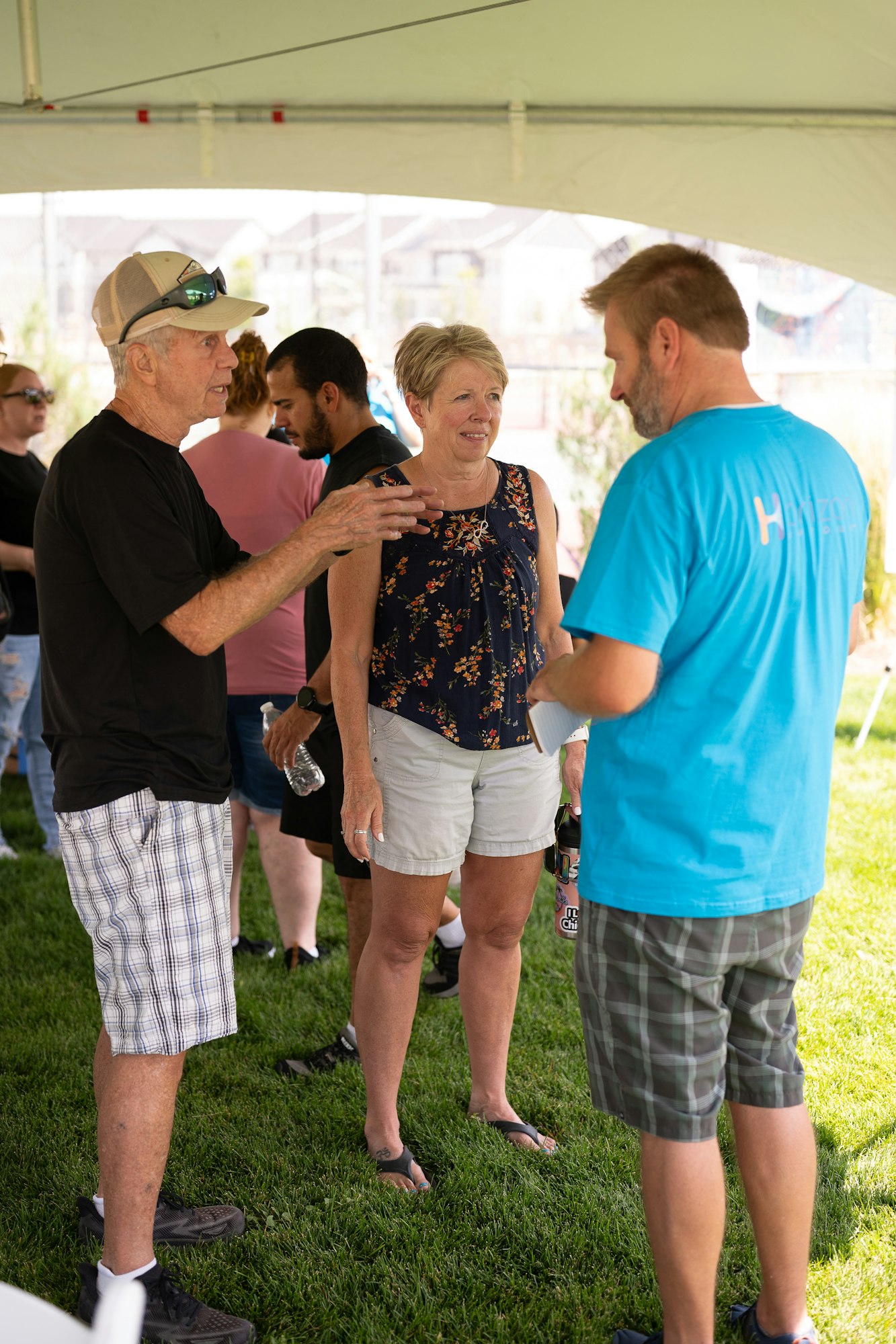A group of people chatting outdoors under a tent, with some holding drinks.