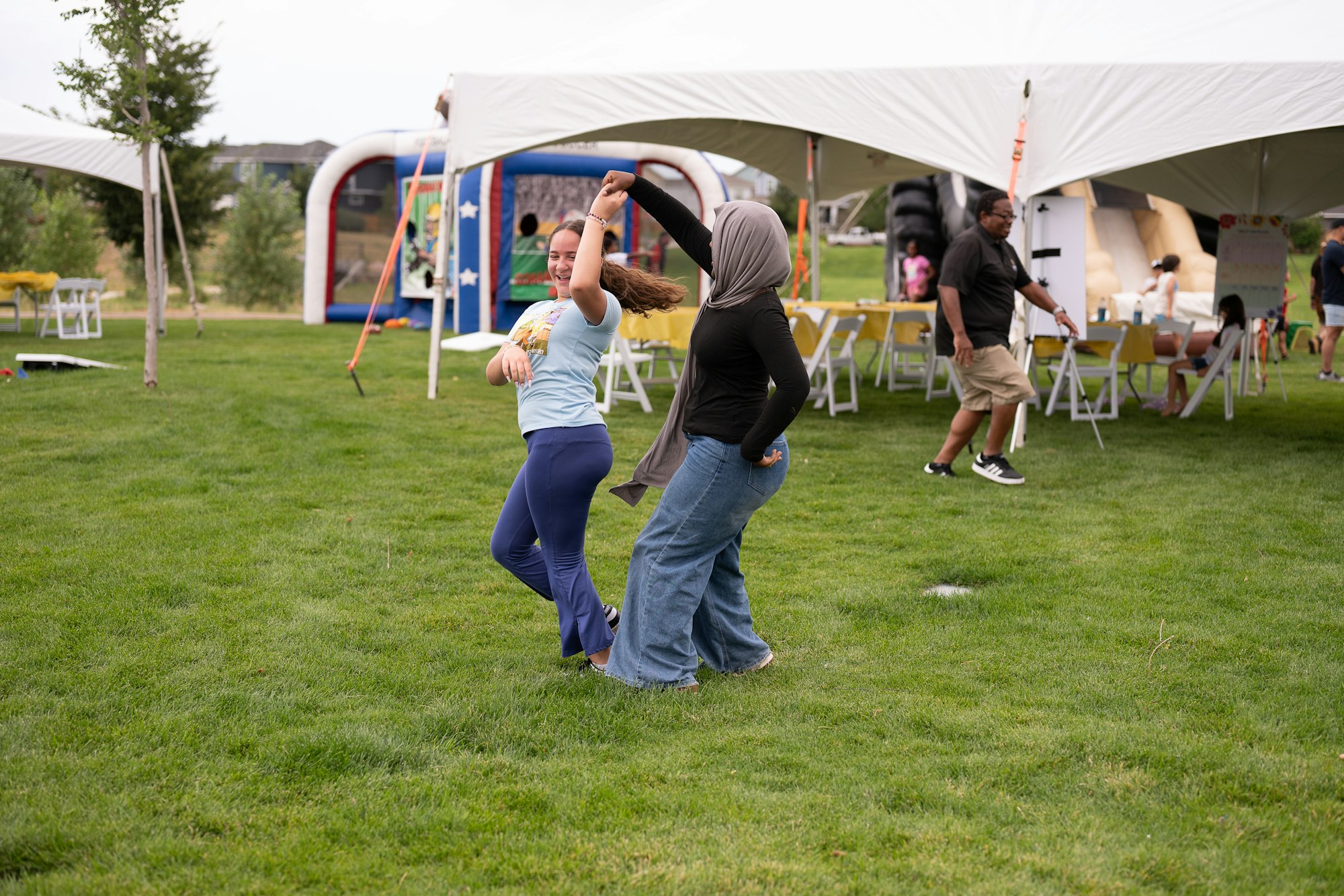 Two people dancing on grass at an outdoor event with tents and a bounce house in the background.