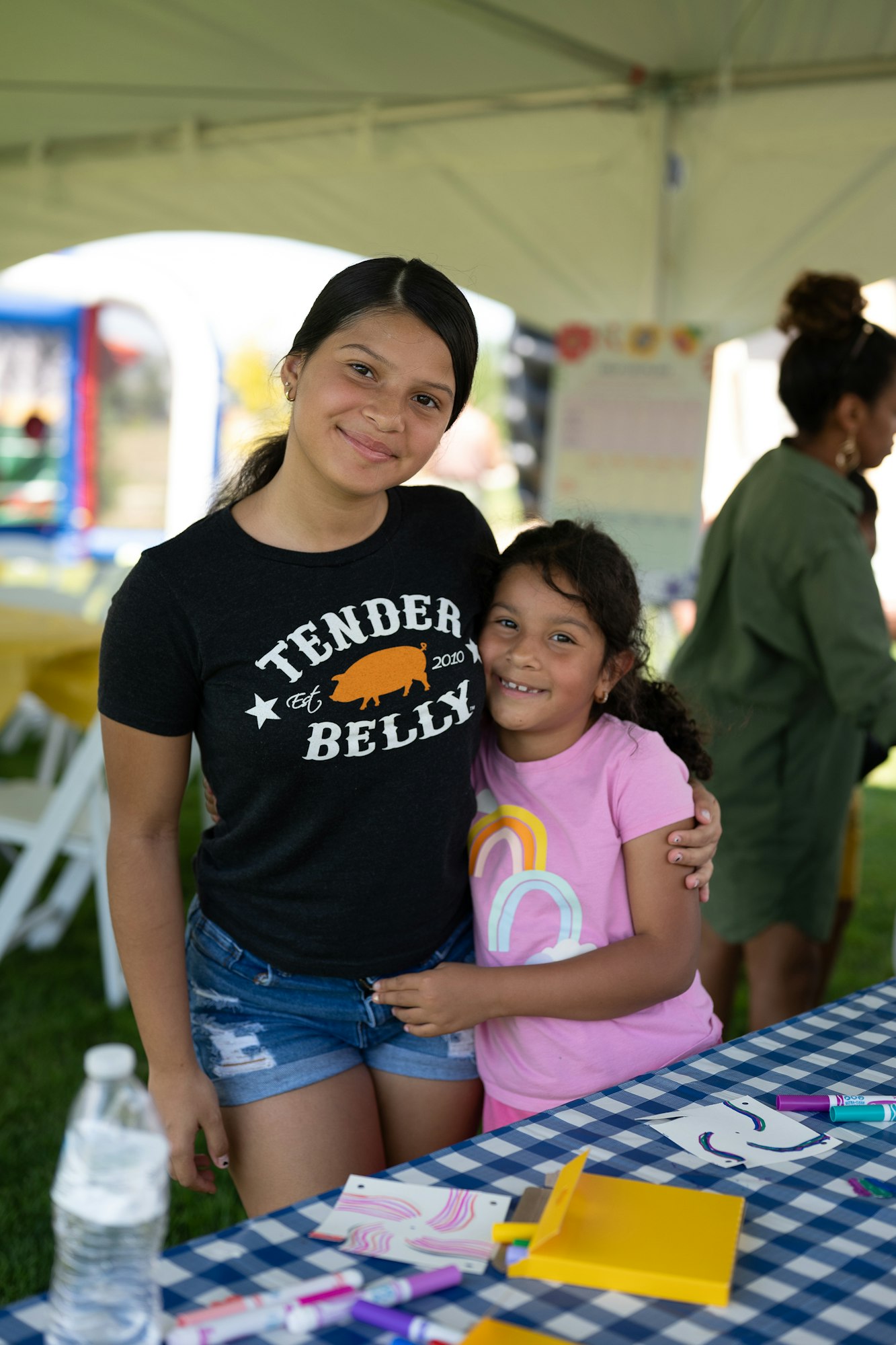 Two people smiling under a tent, with art supplies on a table.