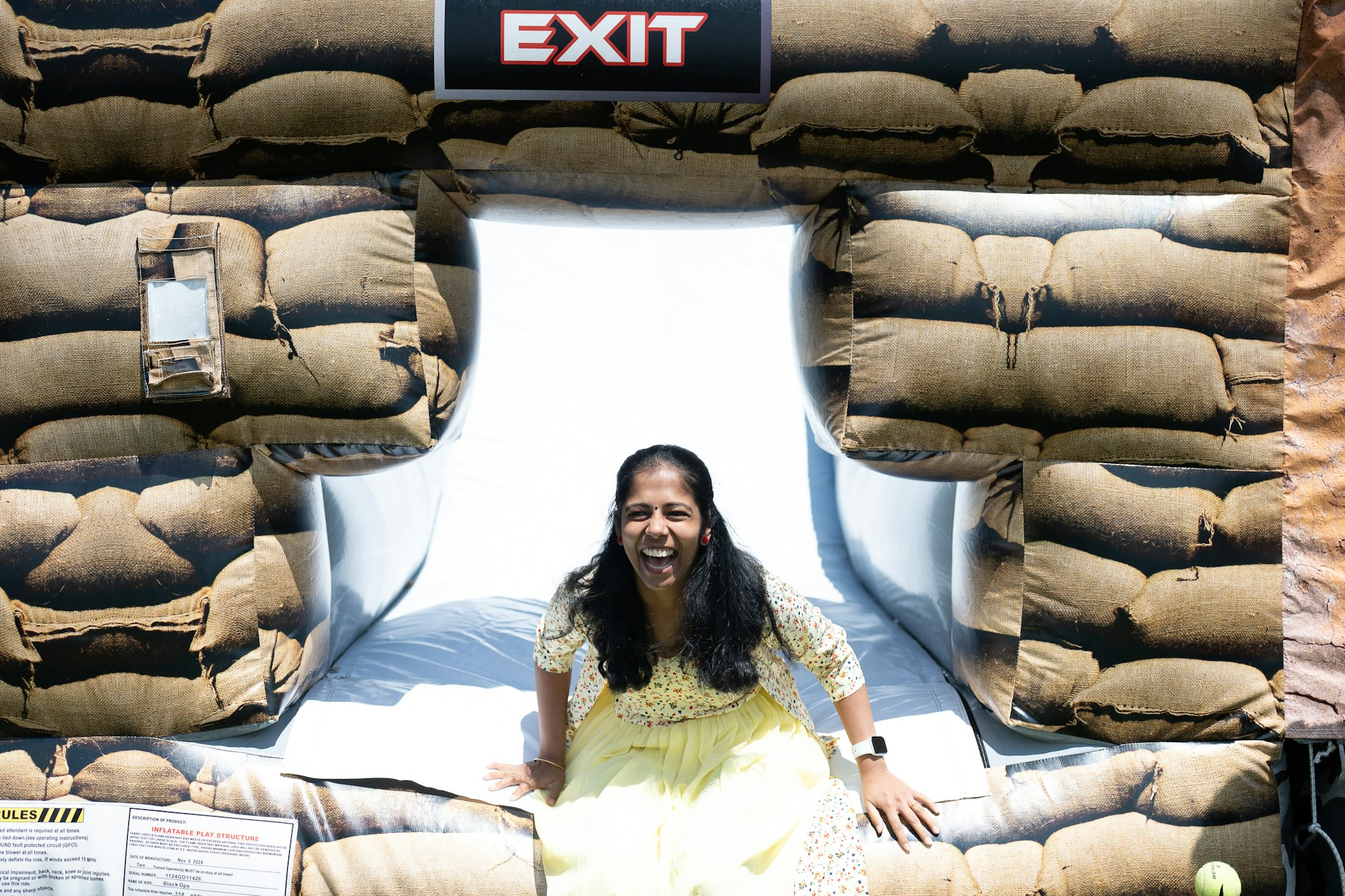 A person laughing while sitting at the exit of an inflatable structure resembling sandbags.