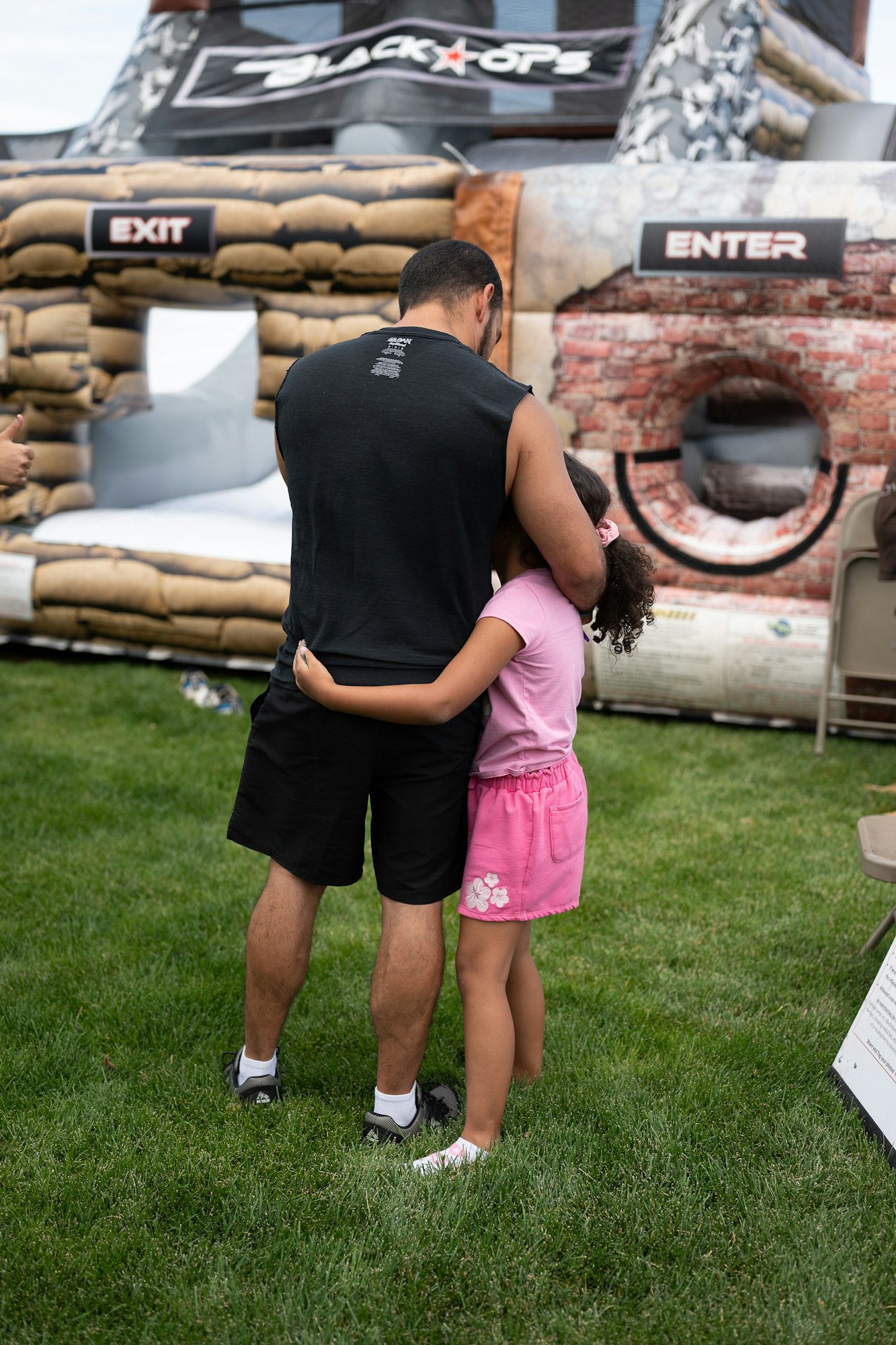 A man and a child hugging in front of an inflatable obstacle labeled "Black Ops" with "Enter" and "Exit" signs.