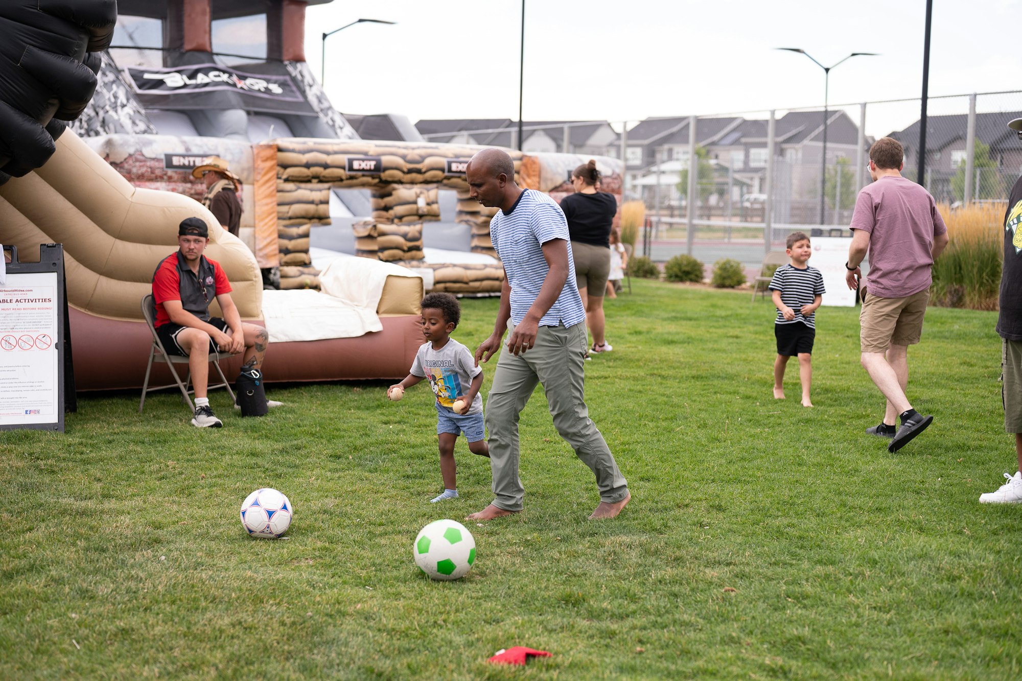 People playing on grass near inflatables, some are kicking soccer balls.