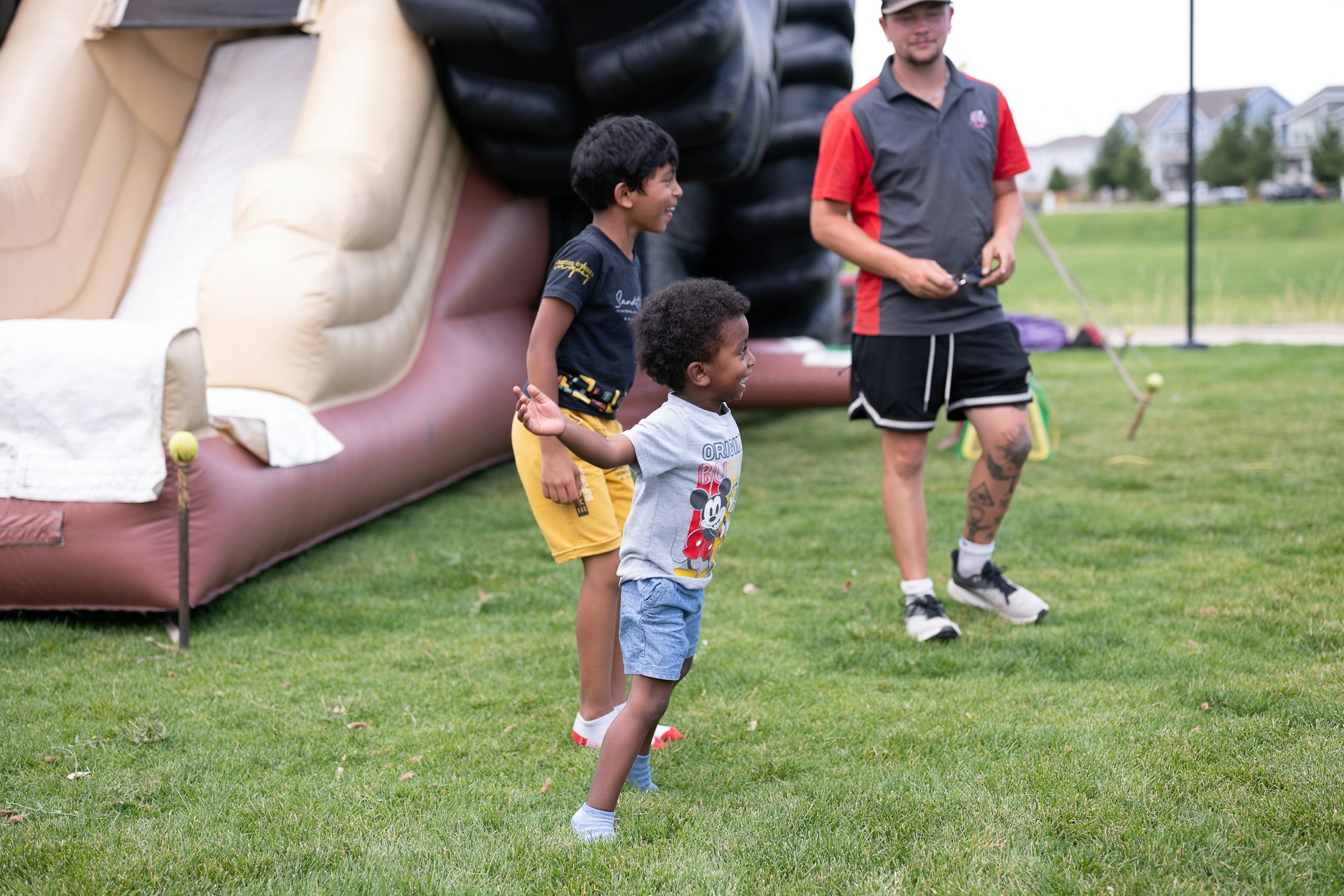 Kids playing near an inflatable slide, supervised by an adult on a grassy field.
