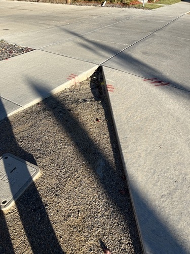Sidewalk and curb intersection with shadows and red markings.