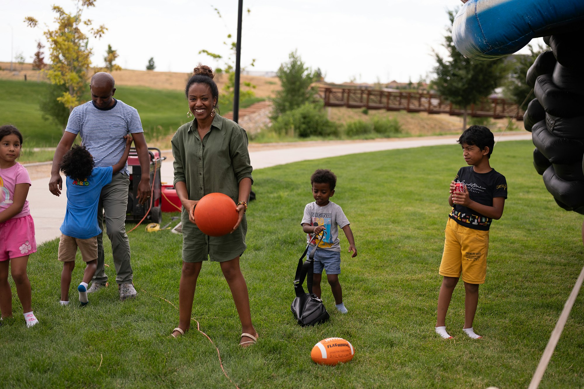 People playing on grass with balls; one person holds a basketball, others have a football and a can.