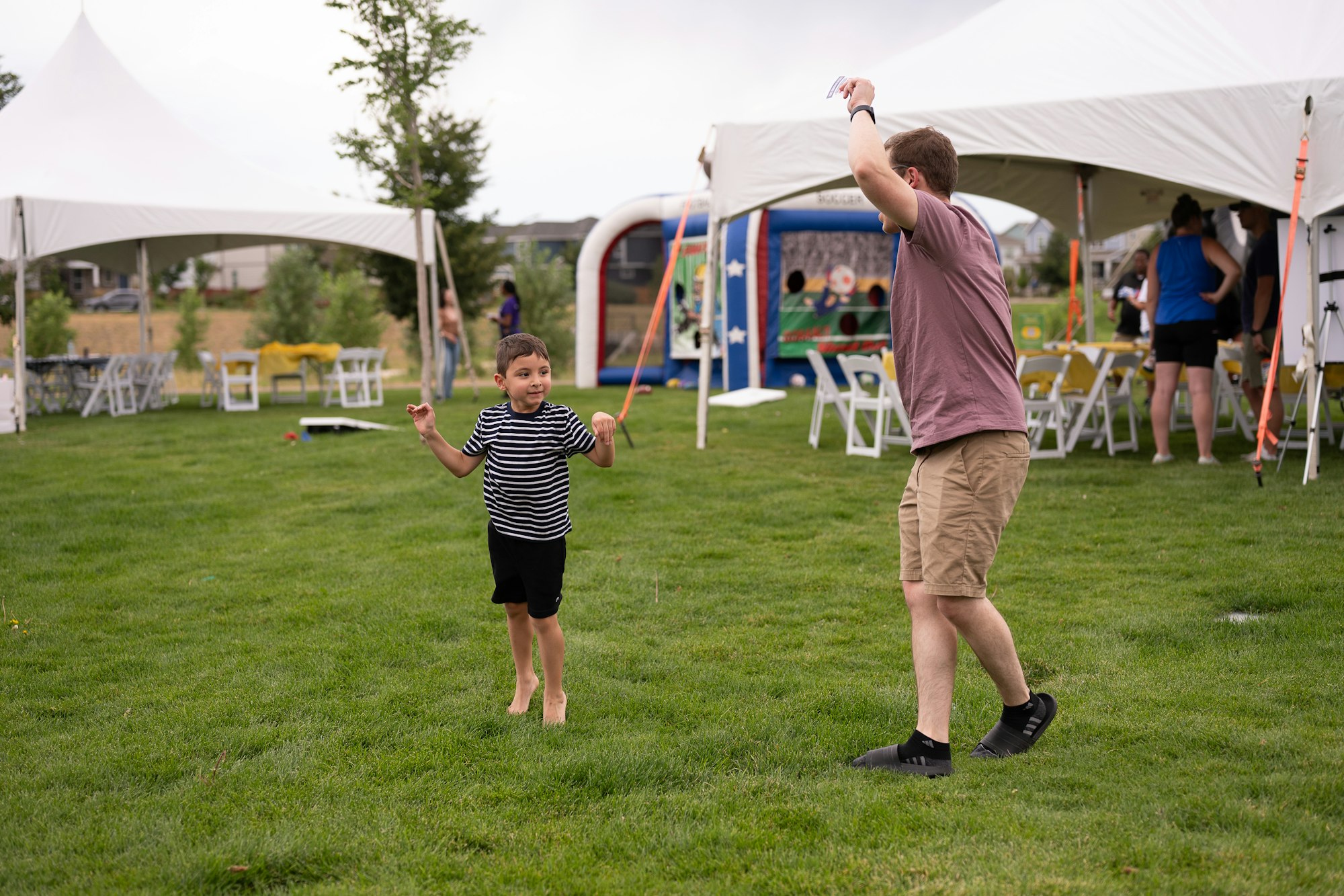 A child and an adult are playing on a grassy area near tents set up for a gathering or event.